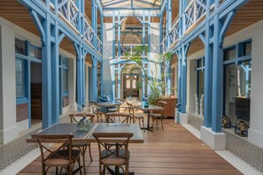 A covered outdoor area with wooden tables and chairs, blue structural elements, and potted plants. - Villa D'Eaux (Villers-sur-Mer)