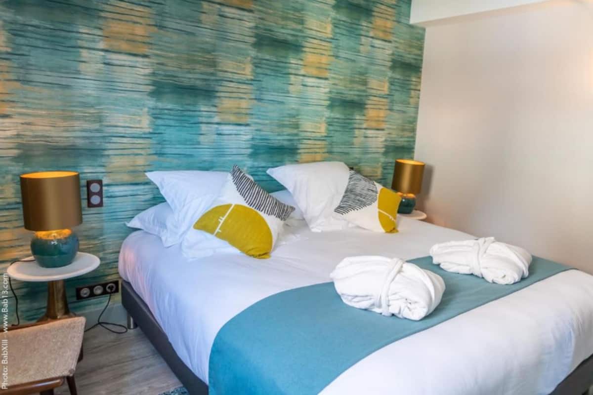 A hotel room with a bed, two bedside lamps, a chair, and a wall with a textured pattern.