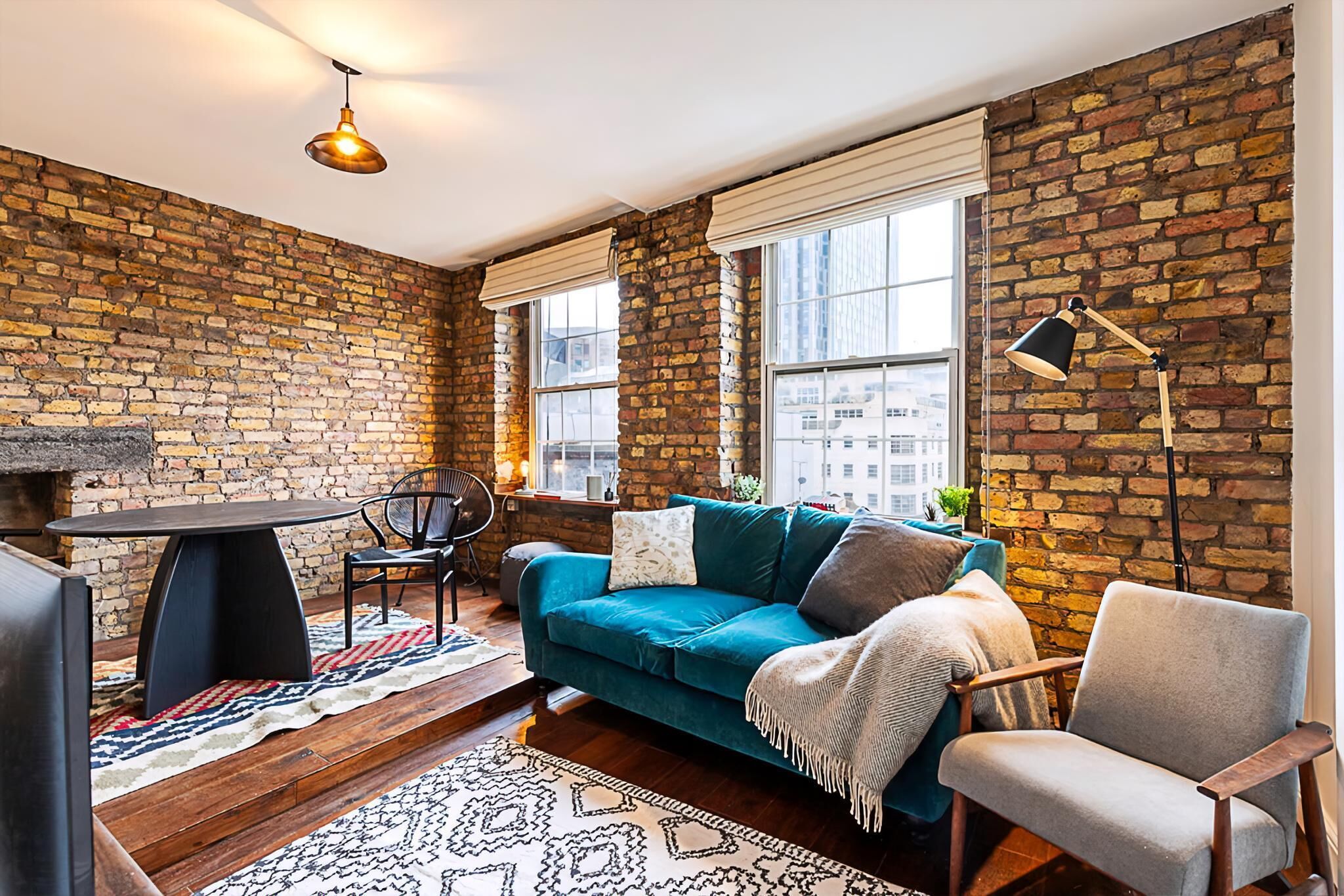 A cozy living room with a brick wall, a teal sofa, a wooden coffee table, and a black floor lamp.