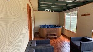 Et overdækket udendørs område med jacuzzi, træterrasse og siddepladser.