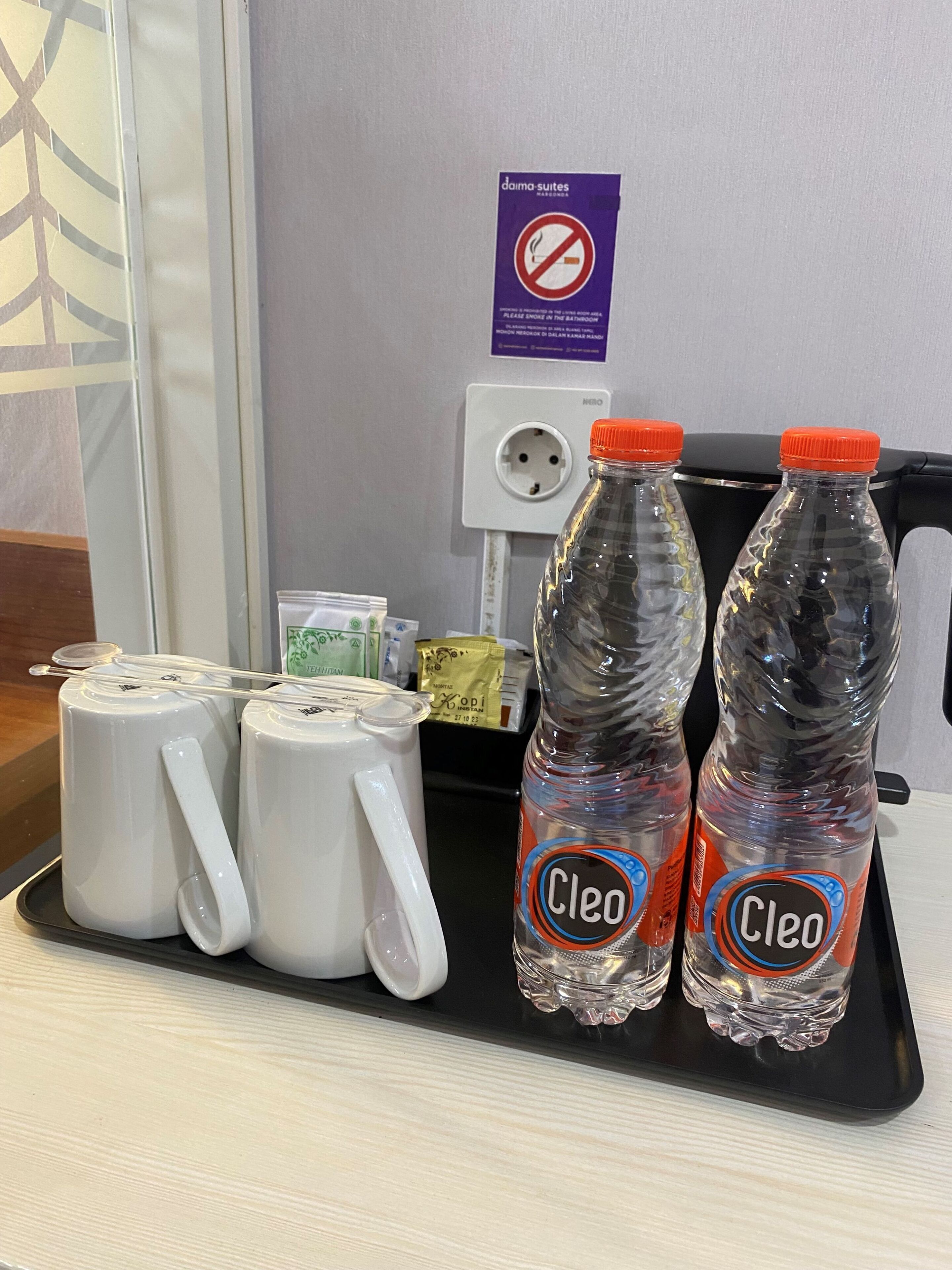 A tray with two bottles of Cleo water, two white mugs, and some packets on a hotel counter.