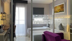 Una habitación de hotel moderna con una cama, un escritorio, un sofá morado y un ventanal con cortinas.