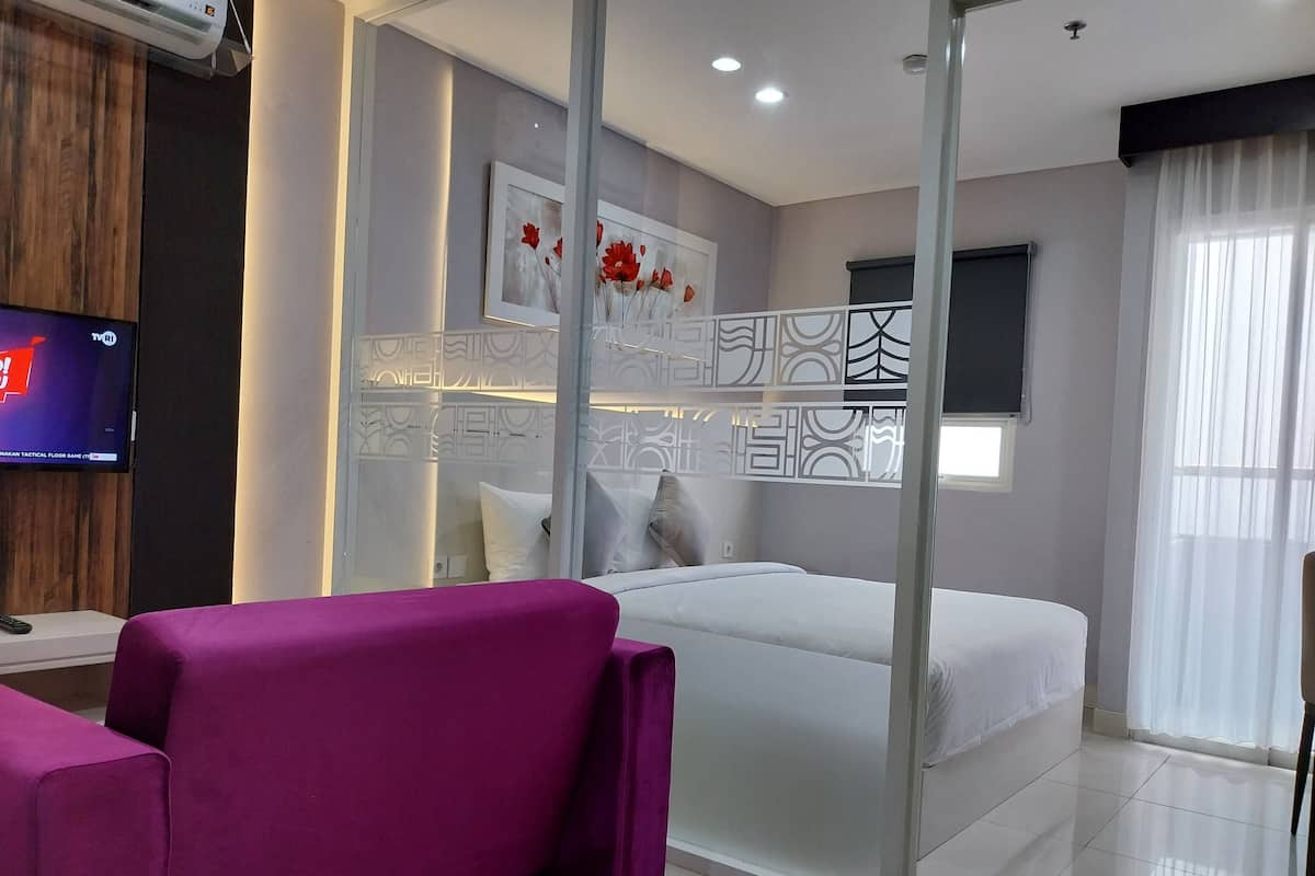 A modern hotel room with a bed, a TV, a decorative wall, and a glass partition.