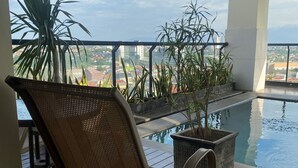 Un balcón con vistas a un paisaje urbano, una piscina y plantas en macetas.