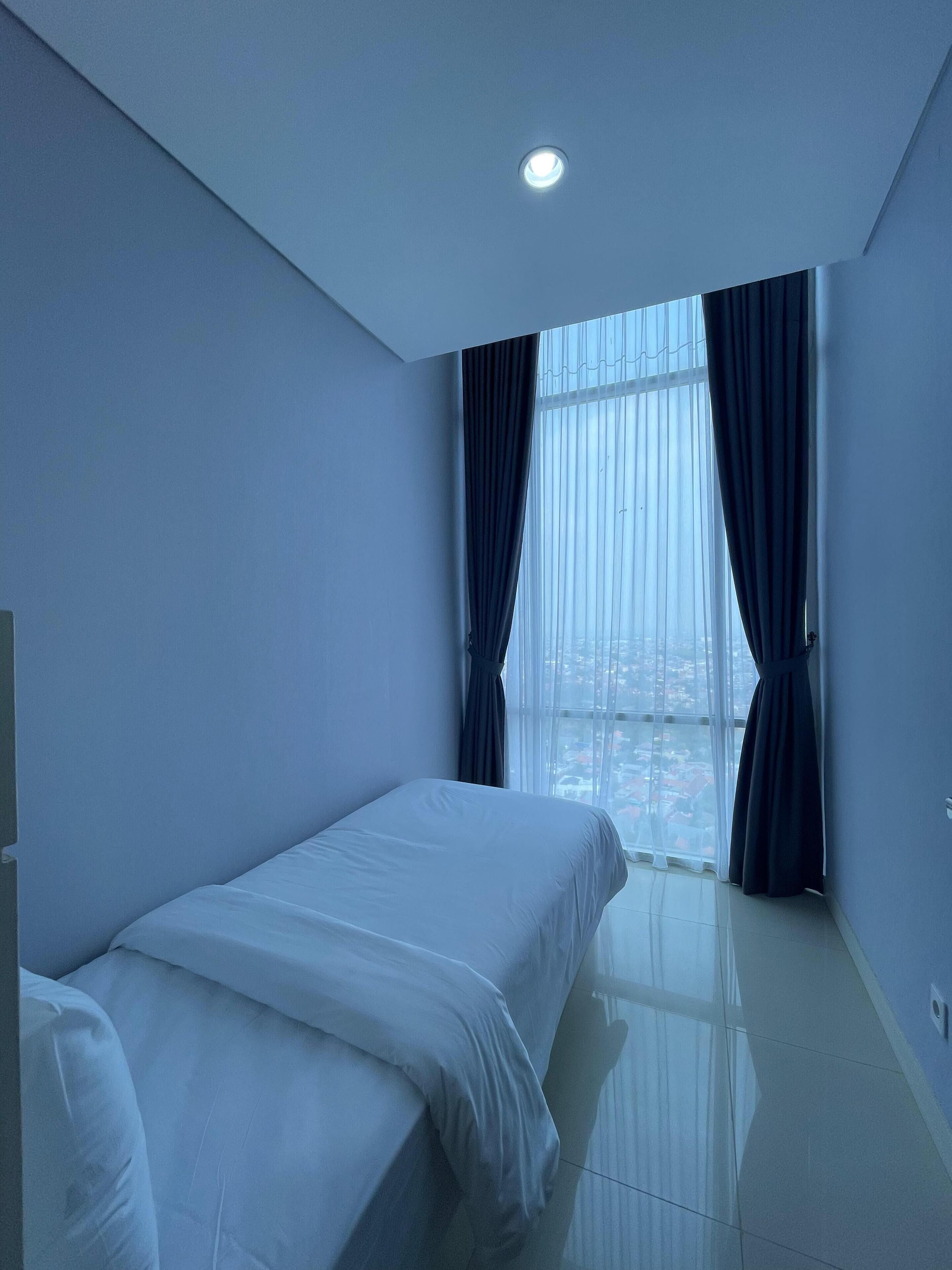 A hotel room with a bed, a window with curtains, and a view of the city.