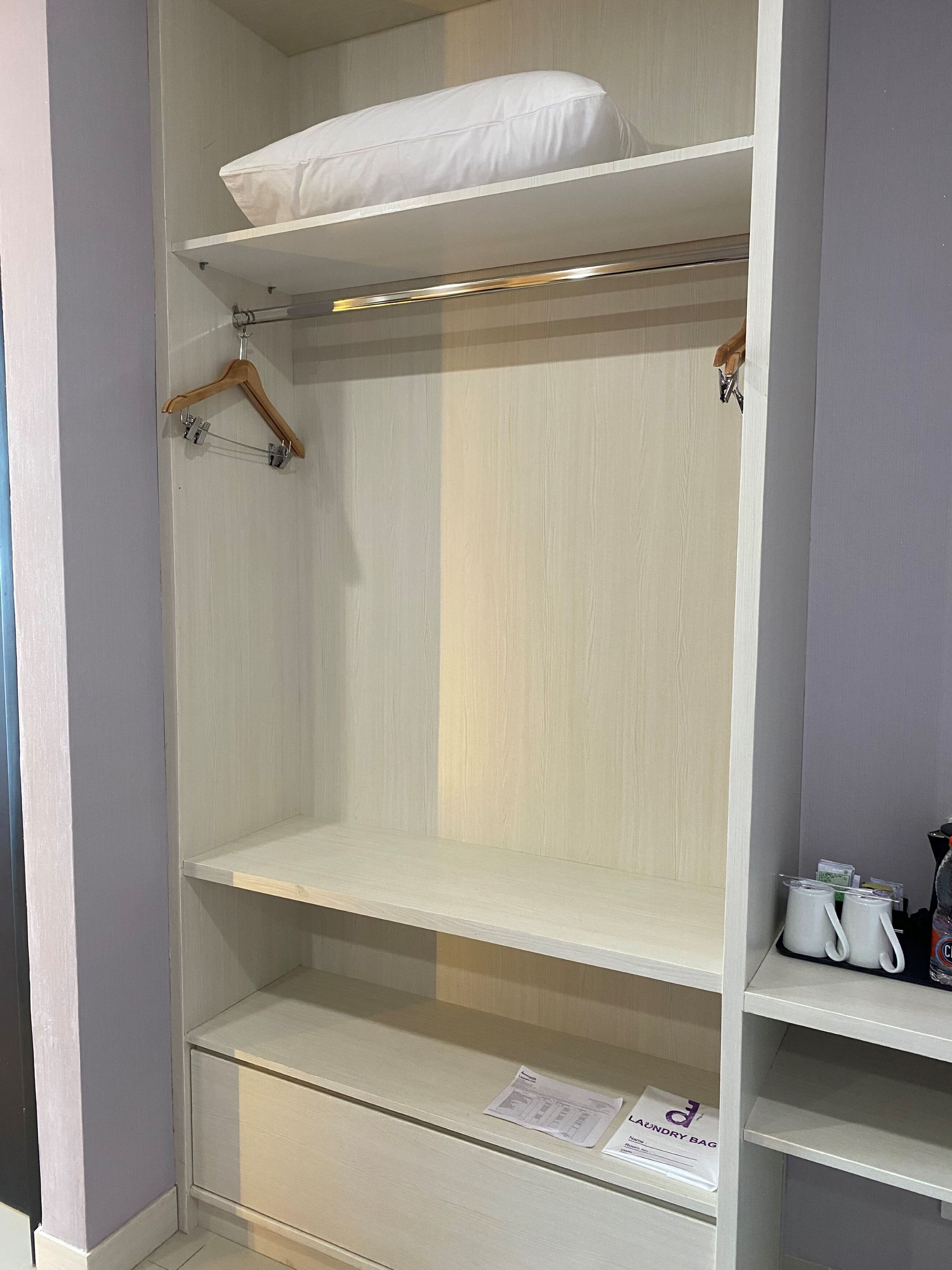 A white wardrobe with multiple shelves, a hanging rod, and a small shelf with items.