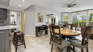 A modern kitchen with a dining area, large windows, and a ceiling fan.