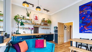 A modern kitchen with wooden cabinets, a blue sofa, and a dining table.
