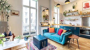 A modern living room with a blue sofa, a coffee table, and a view of the city through large windows.
