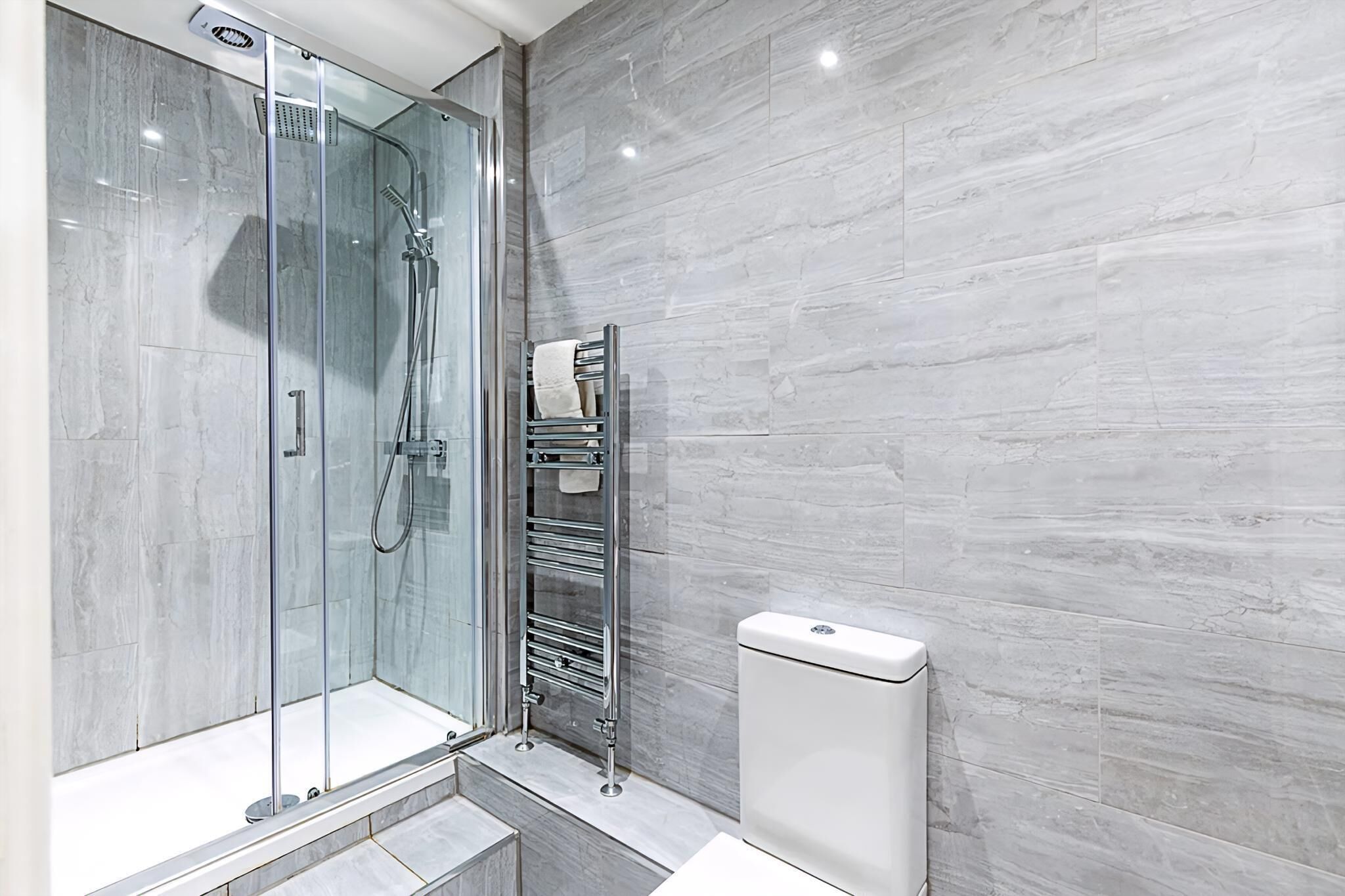 A modern bathroom with a glass-enclosed shower, a white toilet, and a towel rack.