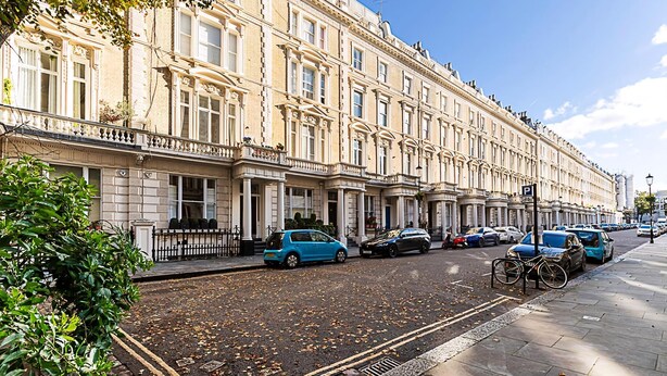 Une rangée de bâtiments de style européen classique, caractérisés par une architecture uniforme, une rue pavée et des voitures garées.