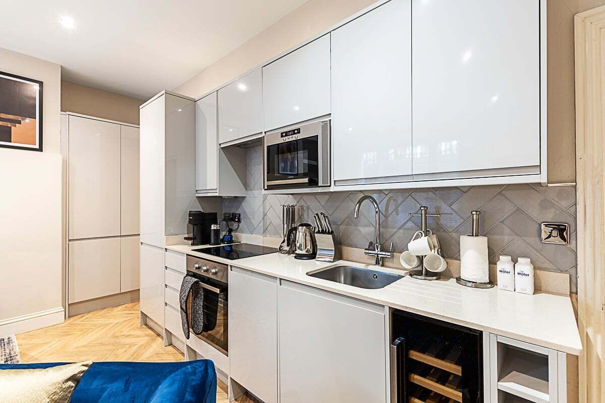 Una cocina moderna con gabinetes blancos, horno empotrado, microondas, fregadero y refrigerador de vinos.