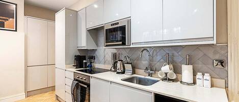 Una cocina moderna con gabinetes blancos, horno empotrado, microondas, fregadero y refrigerador de vinos.
