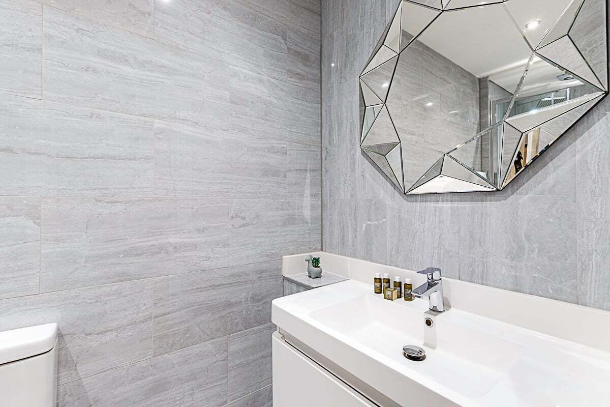 A bathroom with a white sink, a geometric mirror, and a tiled wall.