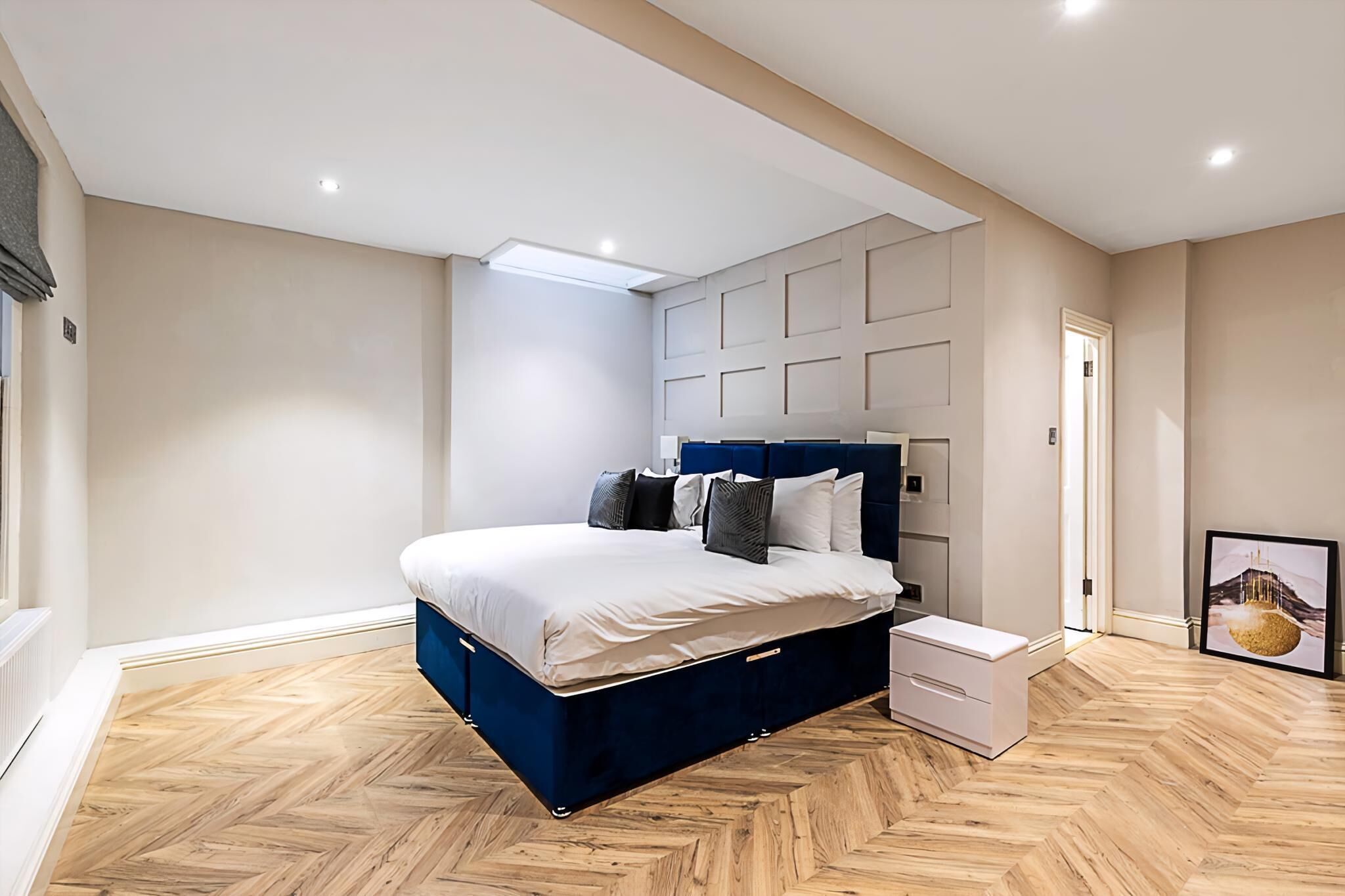 A bedroom with a bed, a nightstand, a dresser, a ceiling light, and a framed picture on the wall.