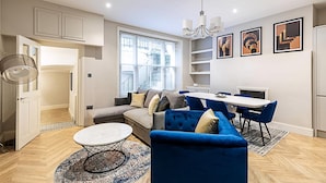 Un salon moderne avec un canapé, des fauteuils bleus, une table à manger et un lustre.