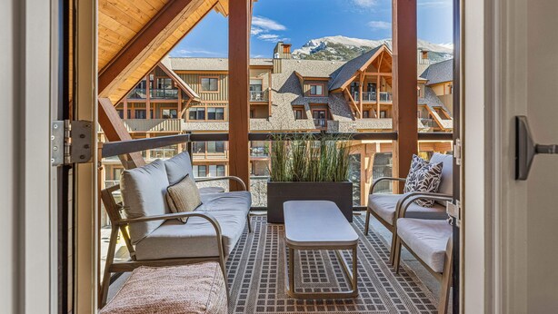 Een balkon met uitzicht op berghuizen, een houten plafond en een zithoek met kussens en een tafel.