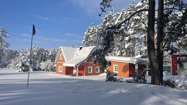 A red building with a snow-covered roof, surrounded by snow-laden trees.