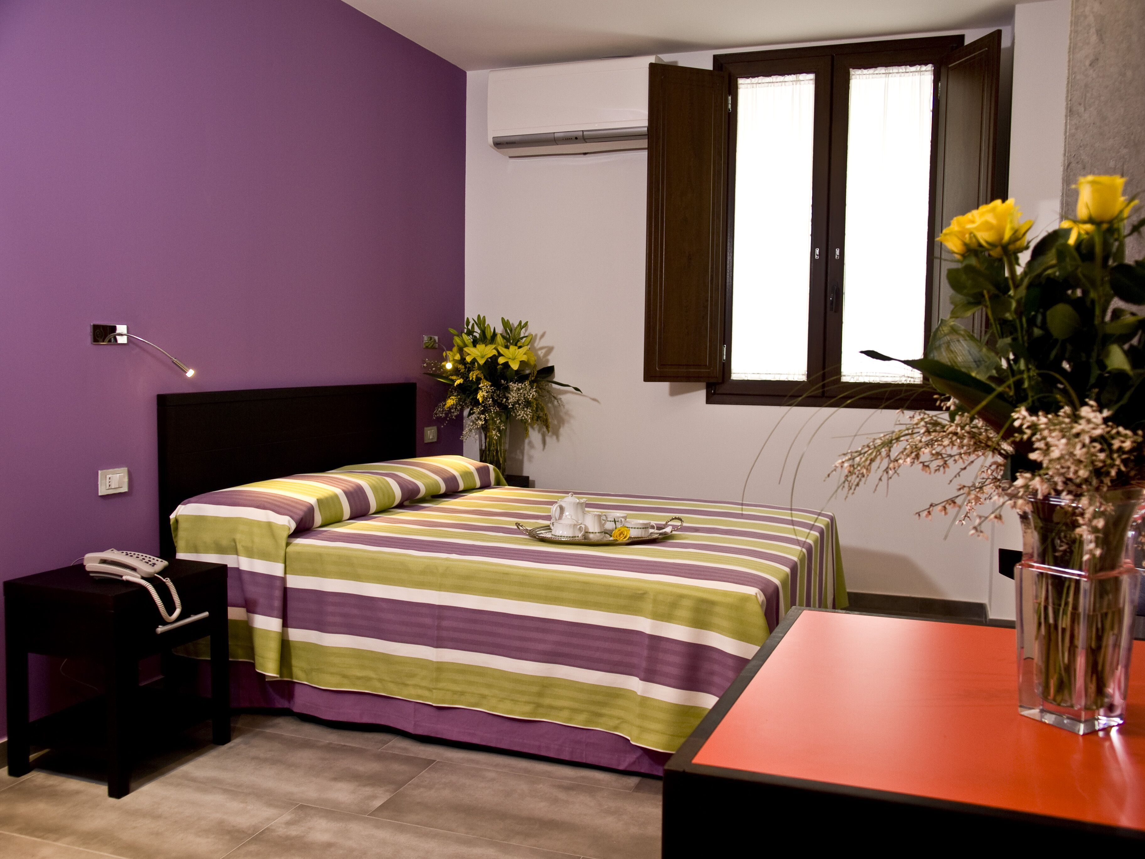A bedroom with a bed, bedside table, nightstand, and a window with curtains.