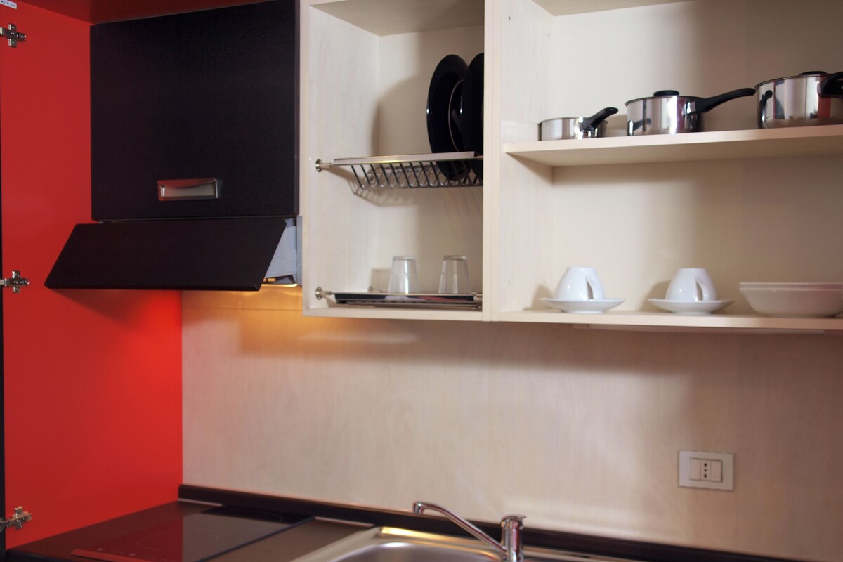 A kitchen with a sink, a red countertop, and shelves with kitchenware.