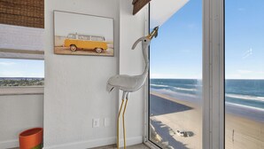 A room with a large window overlooking a beach, a framed picture of a van, and a tall, white sculpture. - Chairman of the Board at White Surf (Daytona Beach)