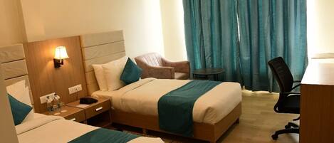 A hotel room with two beds, a desk, a chair, a lamp, and a view of a curtain.
