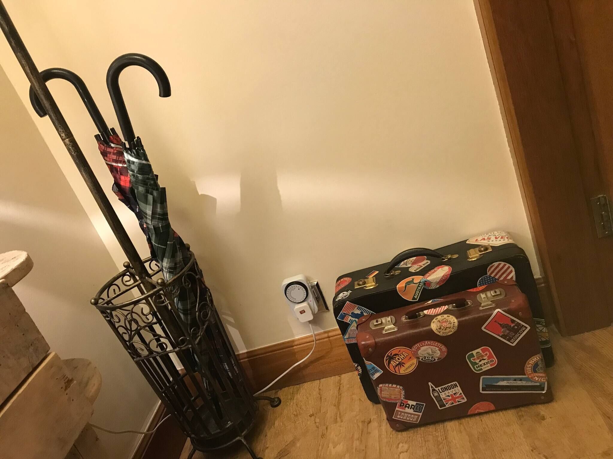 Un plancher en bois, un porte-bagages en métal, un parapluie noir et une valise ornée d’autocollants de voyage.
