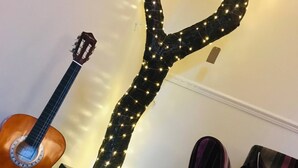 Eine Gitarre, eine dekorative Lichtinstallation, ein Koffer und ein gestreifter Sessel in einem Zimmer.
