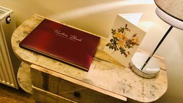 Een houten nachtkastje met een rood boek getiteld ‘Visitor Book’ en een kaartje met een bloemenmotief.