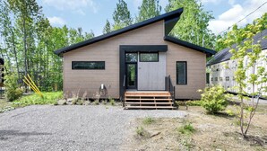 Et moderne hus i to etager med facade i træ, en sort dør og en lille veranda.