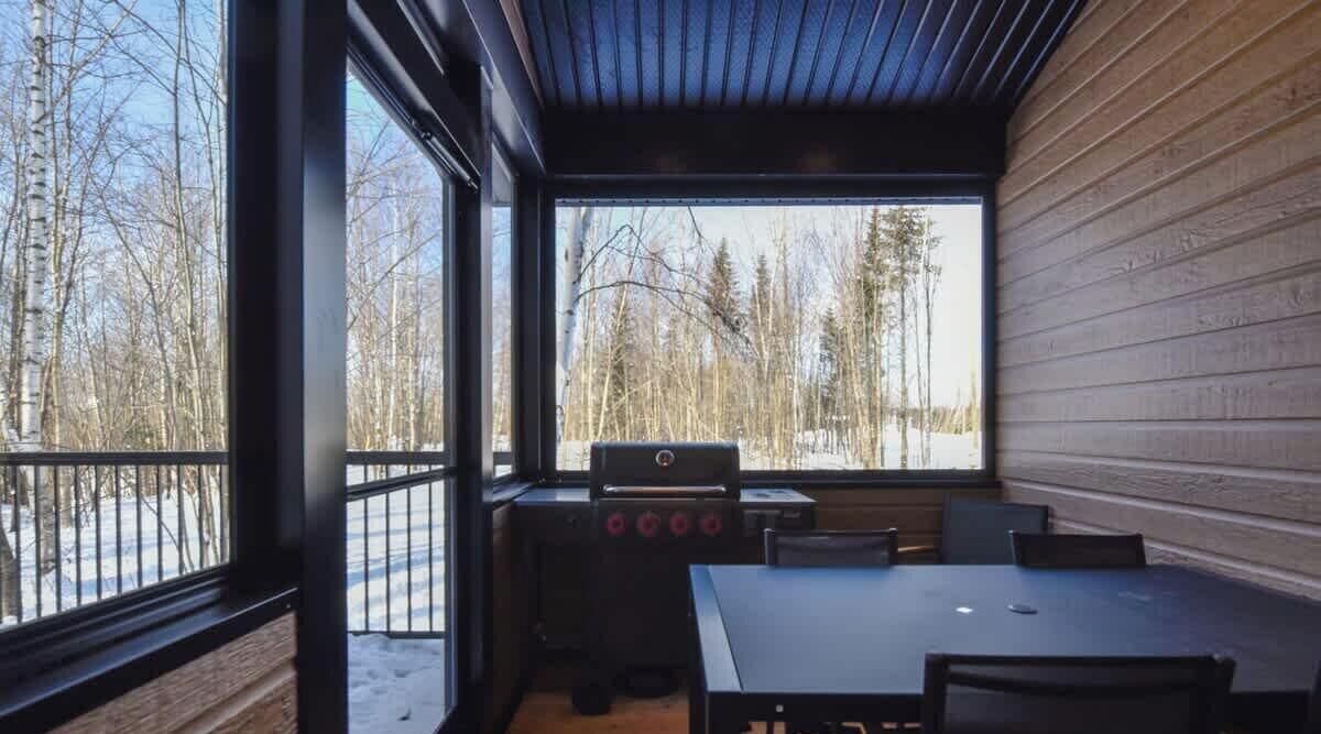 A cabin with a large window, a grill, and a table with chairs.