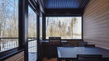 A cabin with a large window, a grill, and a table with chairs.
