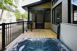 Un bain à remous sur une terrasse en bois, un barbecue et un bâtiment doté de grandes fenêtres.