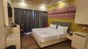 A hotel room with a bed, a desk, a chair, a TV, and a patterned wall. - Shamuka Hotel (Puri)