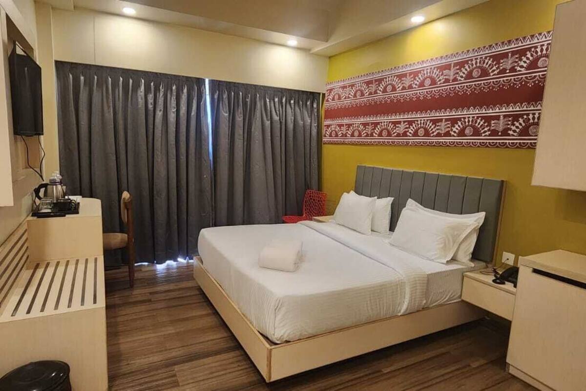 A hotel room with a bed, a desk, a chair, a TV, and a patterned wall.