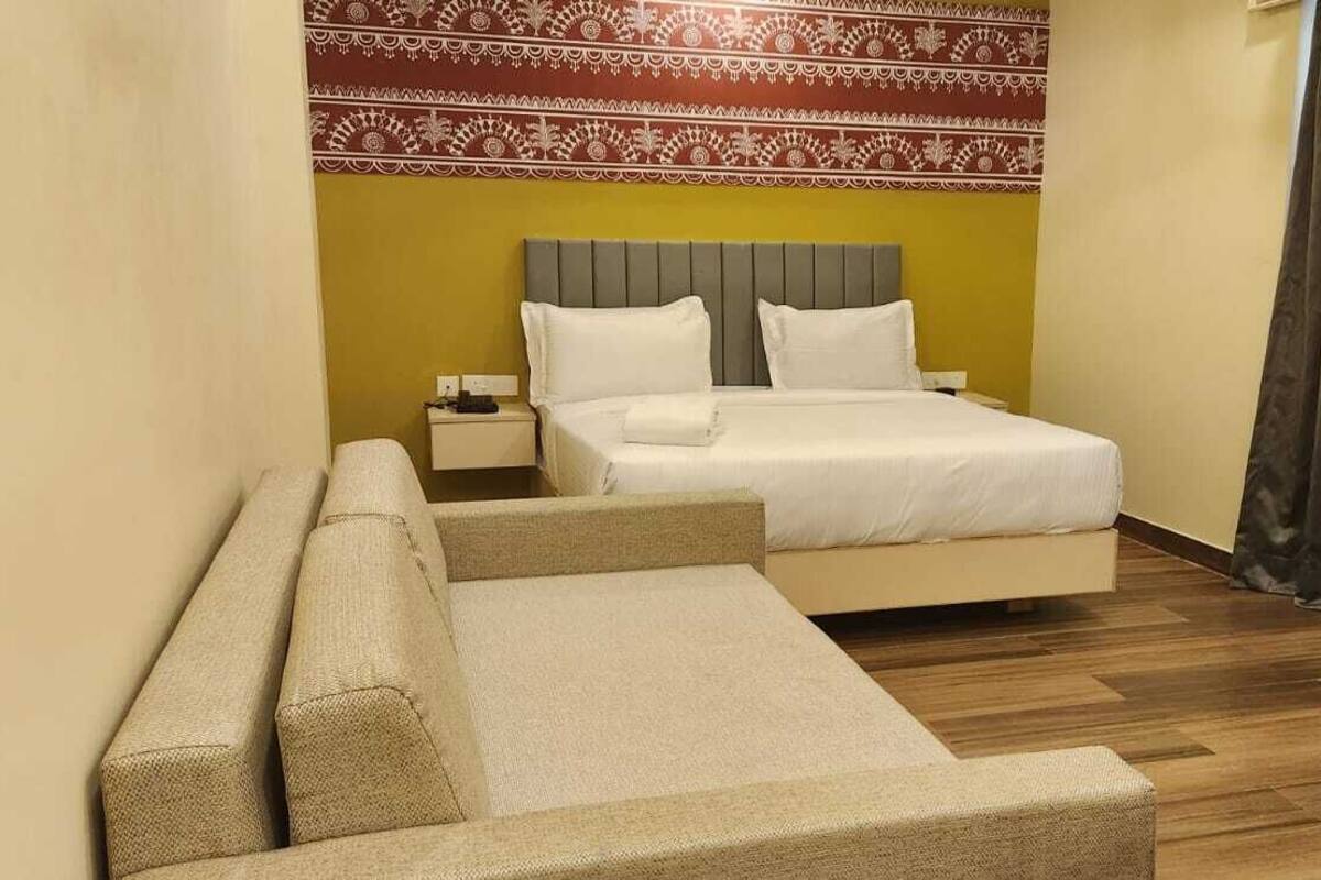A hotel room with a bed, a nightstand, a sofa, and a patterned wall.
