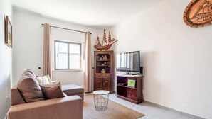 A living room with a sofa, a TV, a wooden cabinet, and a ship model. - Teixeira 's House (Tavira)