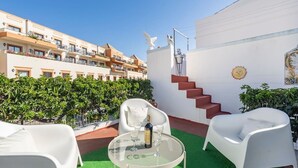 A rooftop terrace with a round table, white chairs, and a bottle of wine. There are steps leading up to a white wall with a sun decoration and a bird sculpture. - Teixeira 's House (Tavira)