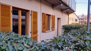 A building with wooden shutters on the windows, a concrete balcony, and a hedge in the foreground.