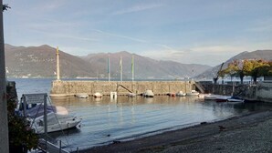 A harbor with boats docked, a lighthouse, and mountains in the background.