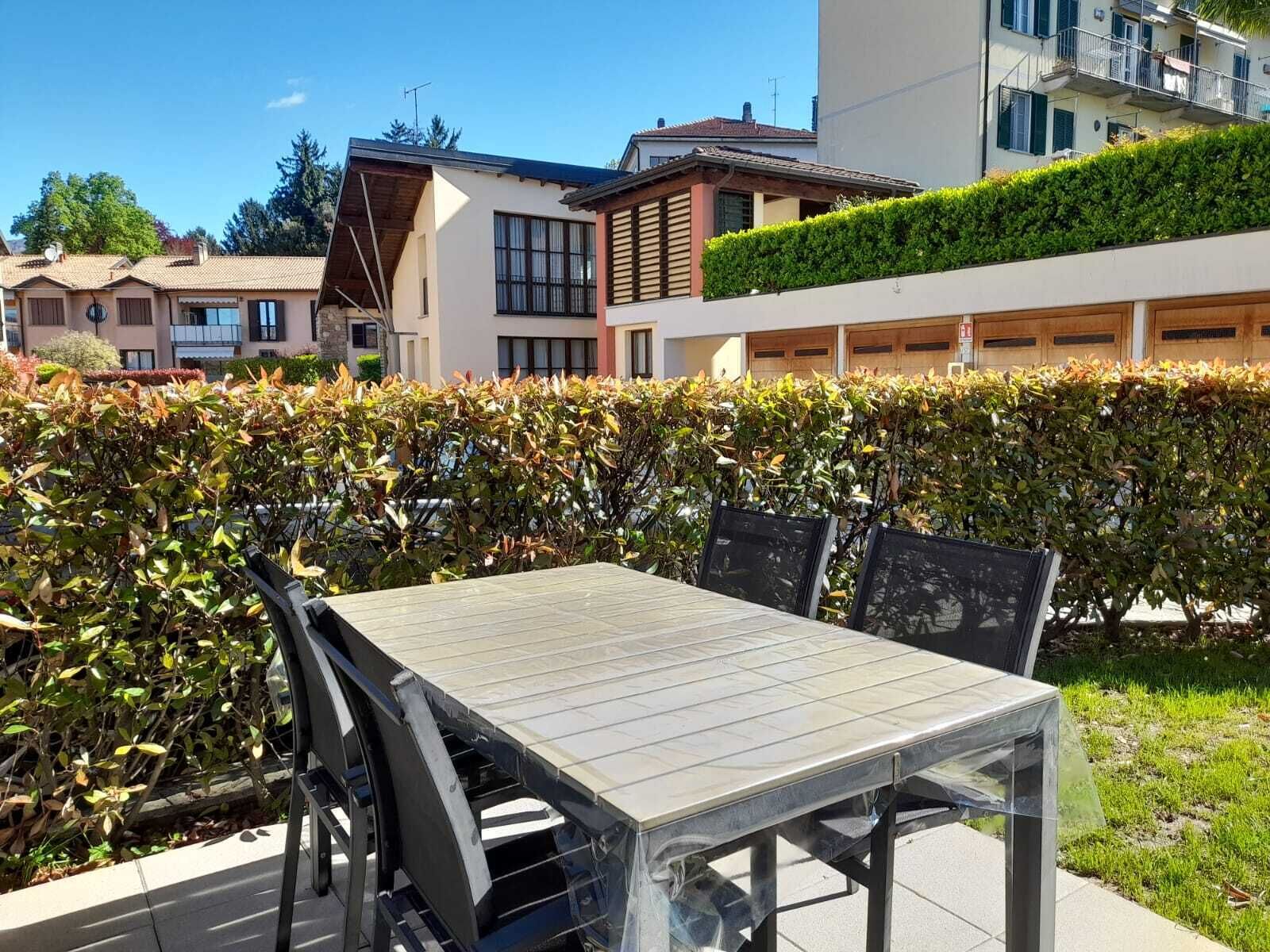 An outdoor patio with a table and chairs, surrounded by a hedge.