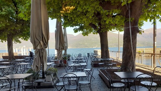An outdoor cafe with tables and chairs, umbrellas, and a view of the water and mountains.