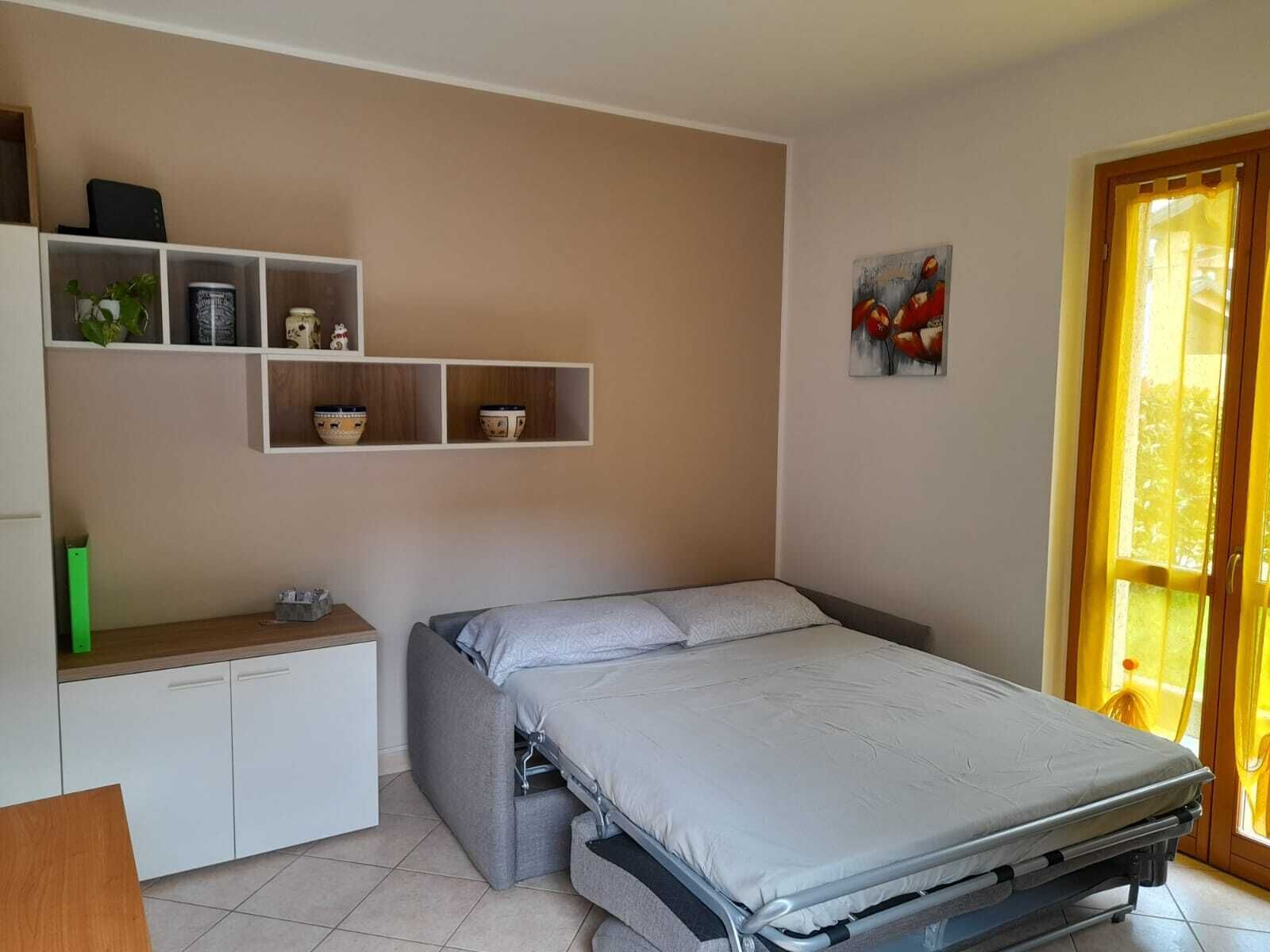 A compact bedroom with a bed, a small desk, and a shelf with decorative items.