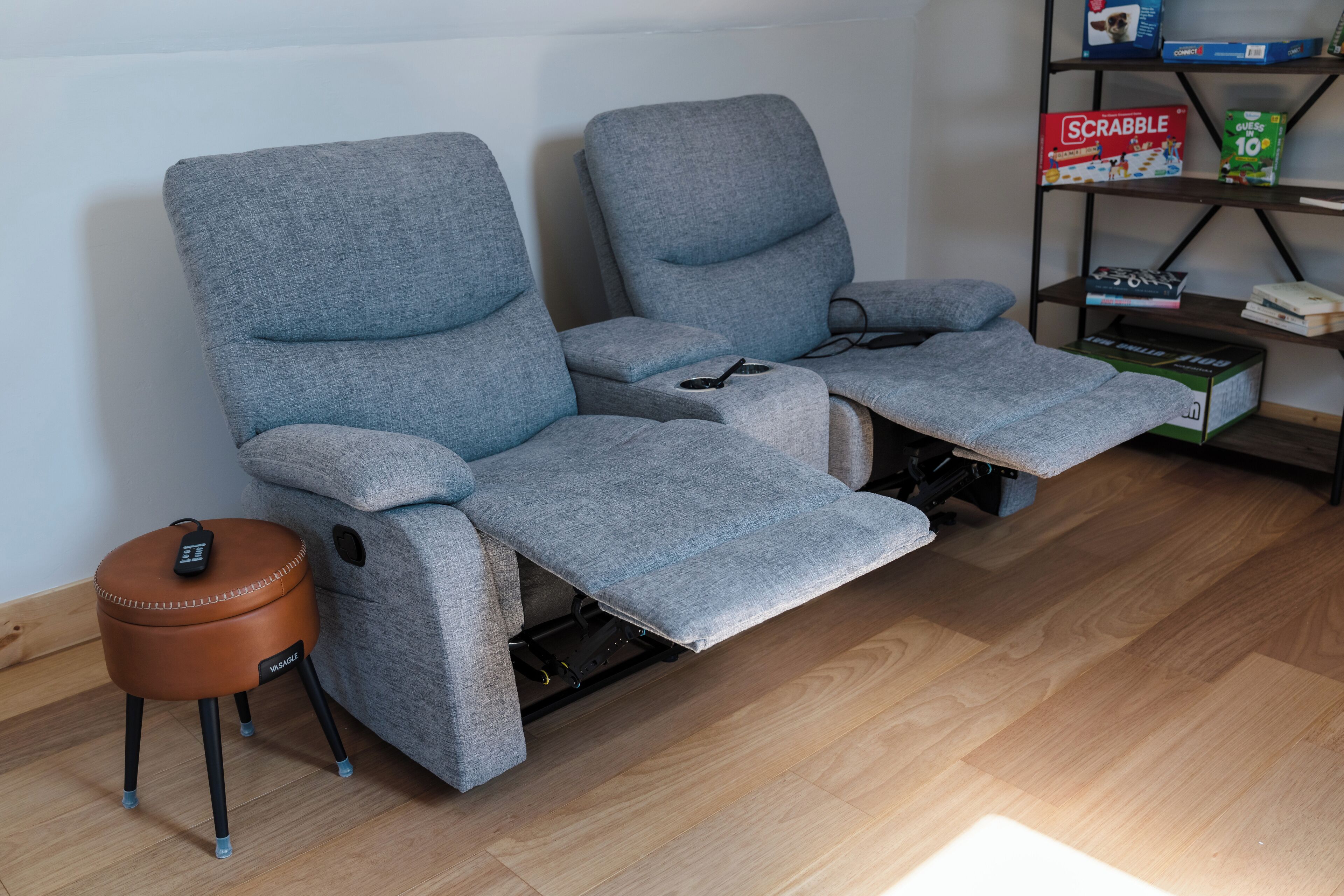 A grey reclining sofa with a footrest and a remote control on a small stool.