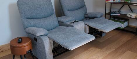 A grey reclining sofa with a footrest and a remote control on a small stool.