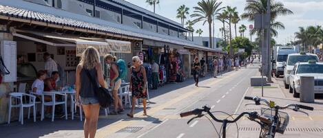 A street with outdoor seating, palm trees, and a bicycle in the foreground.