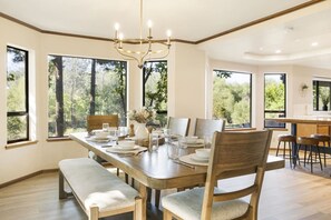 A dining area with a large table, chairs, a bench, and a chandelier.