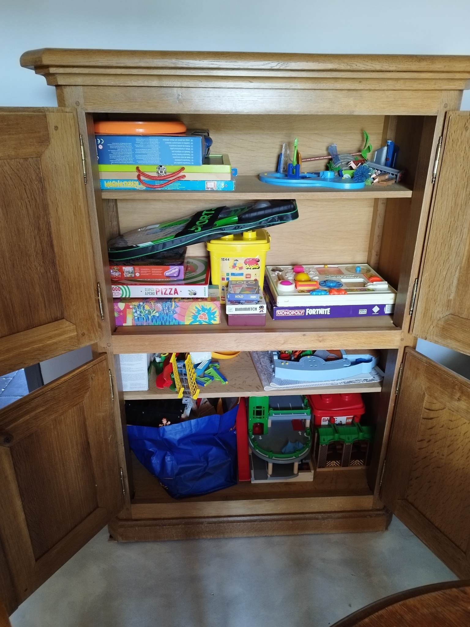 A wooden cabinet with multiple shelves containing various board games and toys.