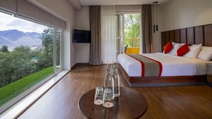 A hotel room with a large bed, a TV, a balcony with a view of mountains, and a round table with glasses. - The Kaal (Leh)