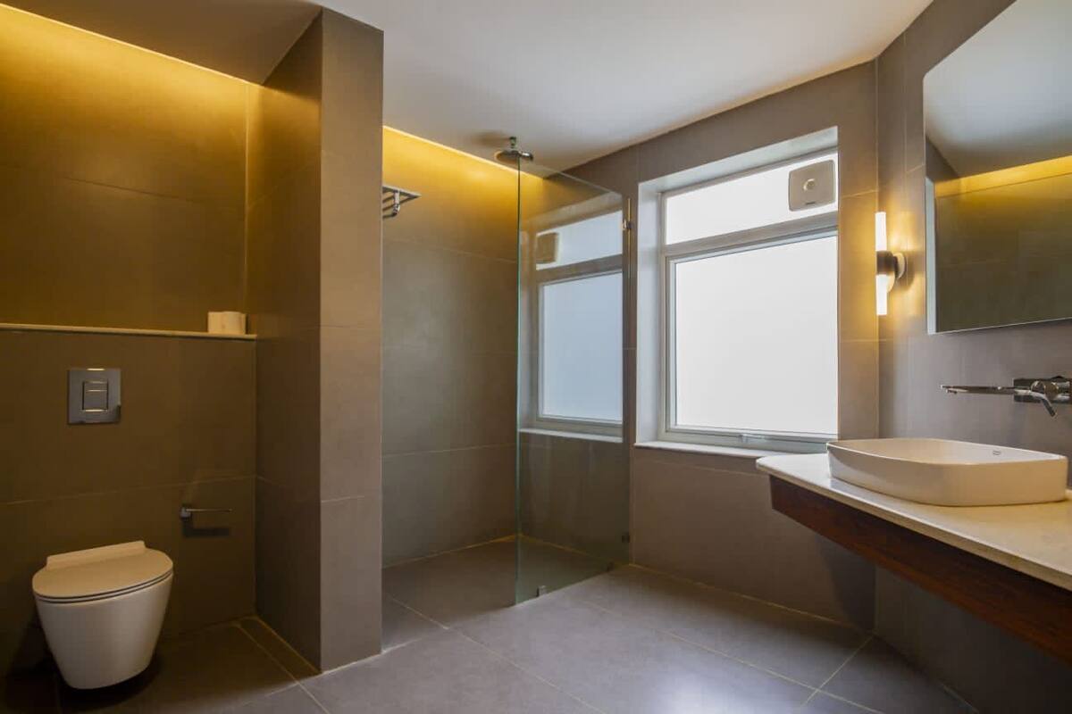 A modern bathroom with a glass-enclosed shower, a toilet, and a sink with a mirror above.